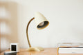 Cream and brass gooseneck desk lamp on a wooden desk