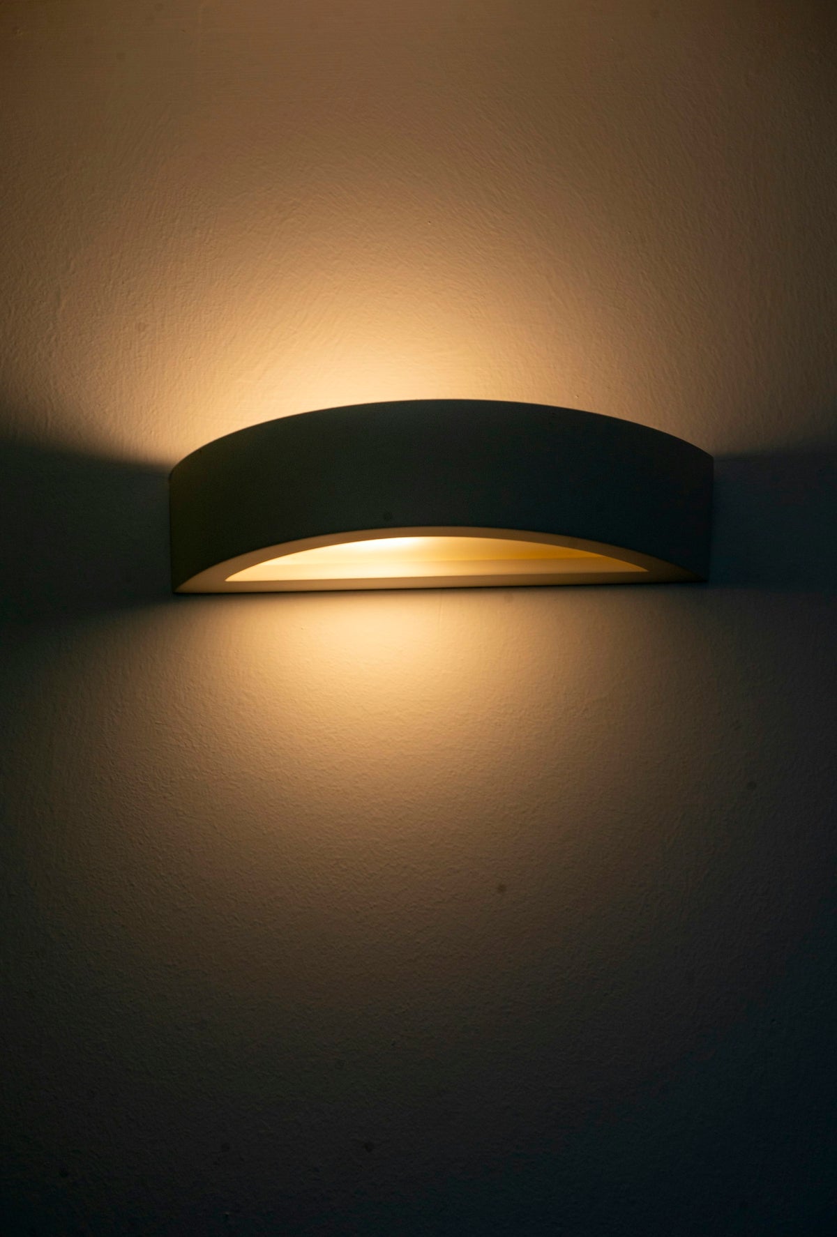 Crescent plaster wall light casting warm light up and down a wall